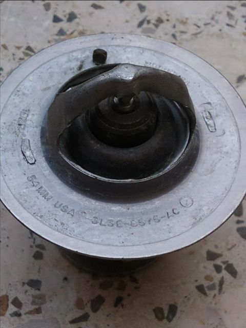 1998 Ford Crown Victoria - A car thermostat is shown, with part numbers and size information visible on its surface.