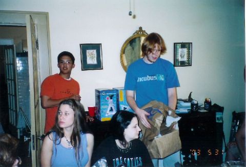 1996 Ford Taurus - A group of people are inside a room, with some standing and others seated, near a table with items on it.