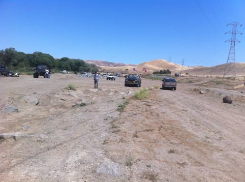 1990 Ford Bronco - Vehicles gather in a dry, open terrain under a clear blue sky, with hills and power lines visible.