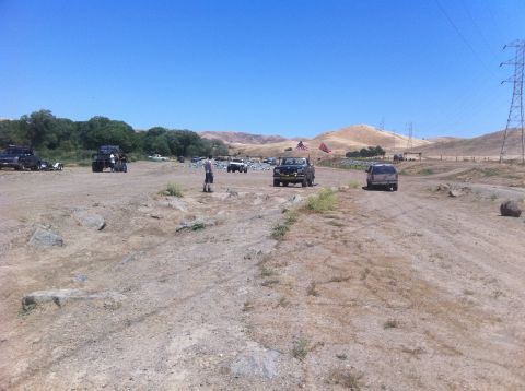 1990 Ford Bronco - Several vehicles are parked and driving in a dry, open area under a clear blue sky.