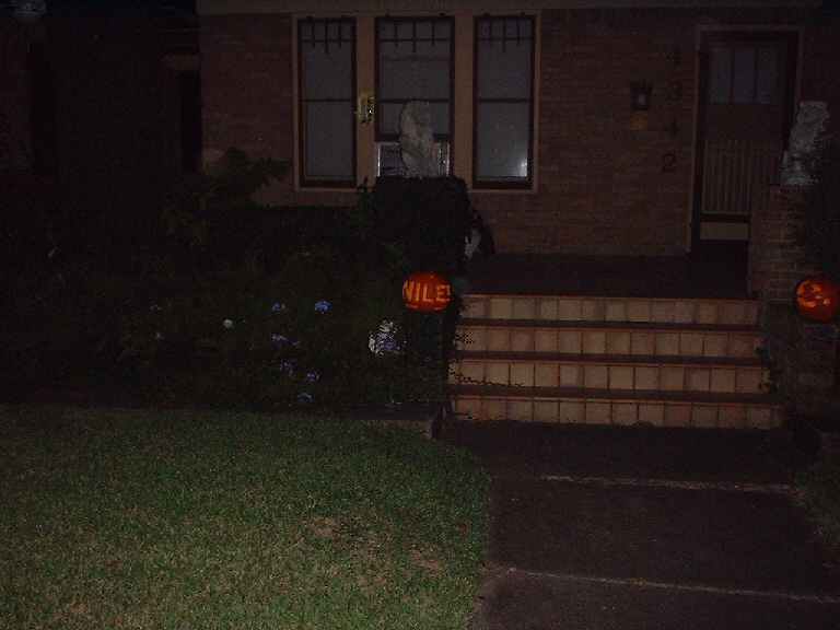 House entrance at night with lit pumpkins on steps and lawn. One pumpkin has 'VILE!' written on it