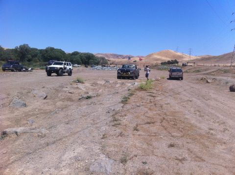 1990 Ford Bronco - Multiple trucks and SUVs are gathered in an outdoor, off-road recreational area under a clear blue sky.