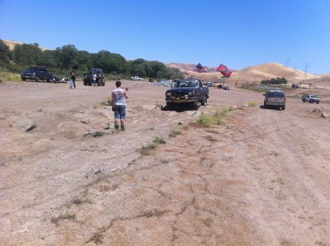 1990 Ford Bronco - Several vehicles are gathered in a dusty outdoor area under a clear blue sky.
