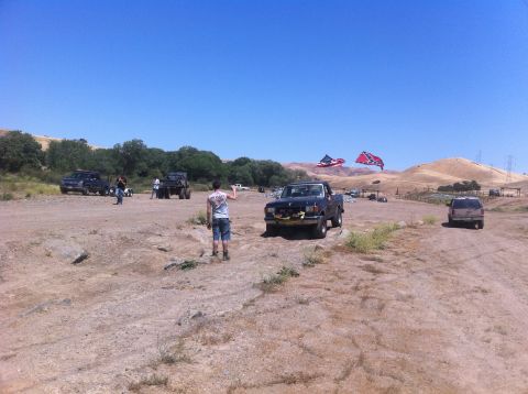 1990 Ford Bronco - A group of vehicles are gathered in a dusty, outdoor area under a clear blue sky.