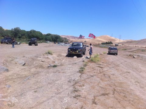 1990 Ford Bronco - Several vehicles are parked and driving in a dusty, outdoor landscape under a clear blue sky.