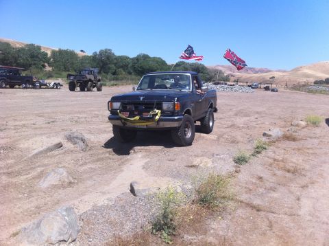 1990 Ford Bronco - A 1990 Ford Bronco is shown with flags flying, parked in a dirt lot with other vehicles.