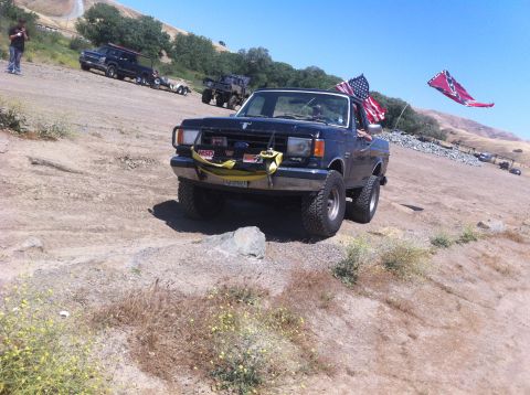 1990 Ford Bronco - A lifted Ford F-series truck is parked on a dirt incline, flying two flags.