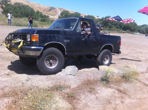 1990 Ford Bronco - A black 1990 Ford Bronco is shown off-road with American flags flying from the rear.