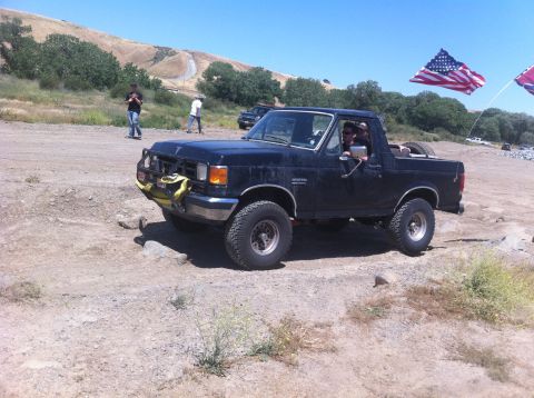 1990 Ford Bronco - Black 1990 Ford Bronco navigates a rocky off-road trail under a clear blue sky.