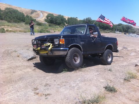 1990 Ford Bronco - A black Ford Bronco is driven off-road, displaying American and Confederate flags.