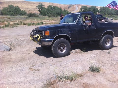 1990 Ford Bronco - A black Ford Bronco is seen off-road with an American flag flying from the back.