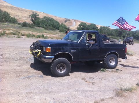 1990 Ford Bronco - A black Ford Bronco is parked on a dirt road with an American flag flying from the back.
