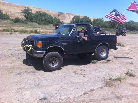 1990 Ford Bronco - A black Ford Bronco with American and Confederate flags flies past on a dusty trail.