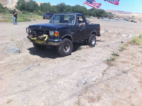 1990 Ford Bronco - 1990 Ford Bronco modified for off-road use, seen with flags in a dry, outdoor setting.