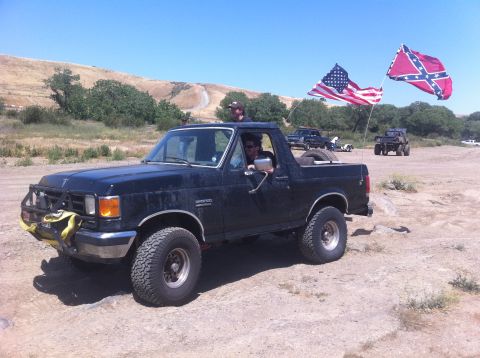 1990 Ford Bronco - Black 1990 Ford Bronco with two flags flying in a dusty, outdoor setting.
