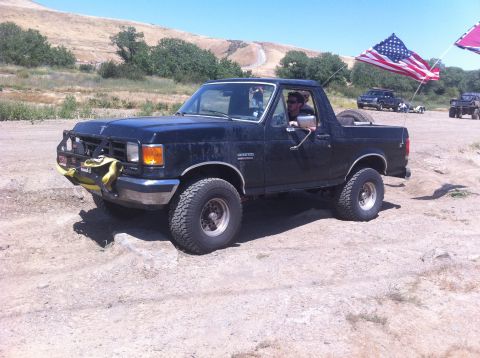 1990 Ford Bronco - This black Ford Bronco, likely from the late 1980s, is seen off-road with an American flag flying from its antenna.
