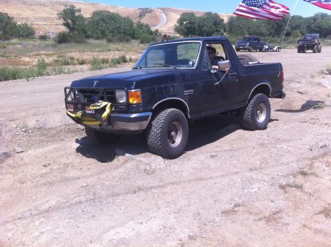 1990 Ford Bronco - A black 1990 Ford Bronco is seen off-road with American flags flying.