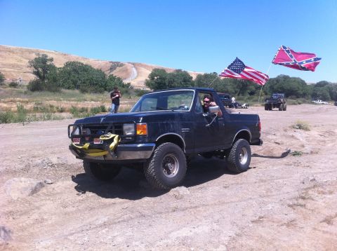 1990 Ford Bronco - A black 1990 Ford Bronco is seen off-road with two flags flying from its rear.