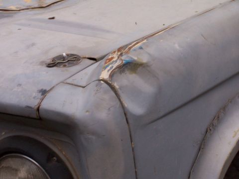 1973 Ford Bronco - Weathered vehicle front fender and hood show damage and a hood pin.