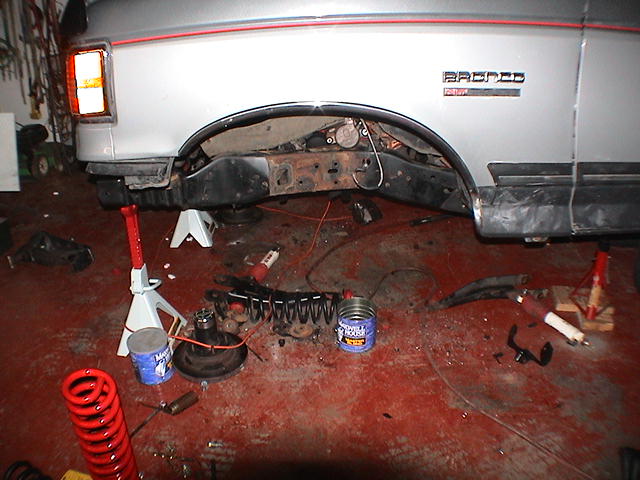 Silver Ford Bronco rear on jack stands, wheel removed, coil springs and brake drum on garage floor