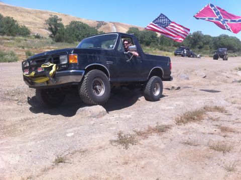 1990 Ford Bronco - This 1990 Ford Bronco navigates rocky terrain, accompanied by two flags in the background.