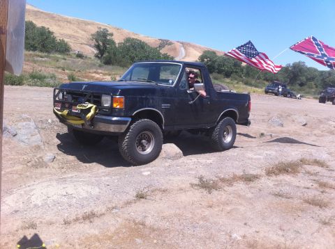 1990 Ford Bronco - A black Ford Bronco with a brush guard and flags is seen off-road.