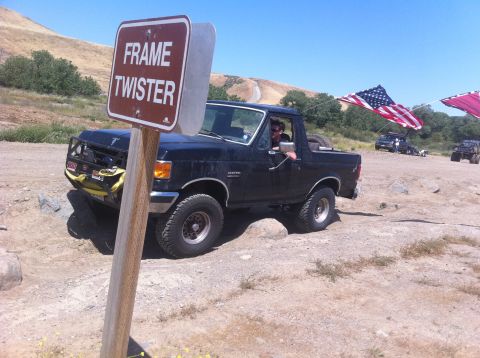 1990 Ford Bronco - Black 1990 Ford Bronco tackles an off-road obstacle course, with other vehicles visible in the background.