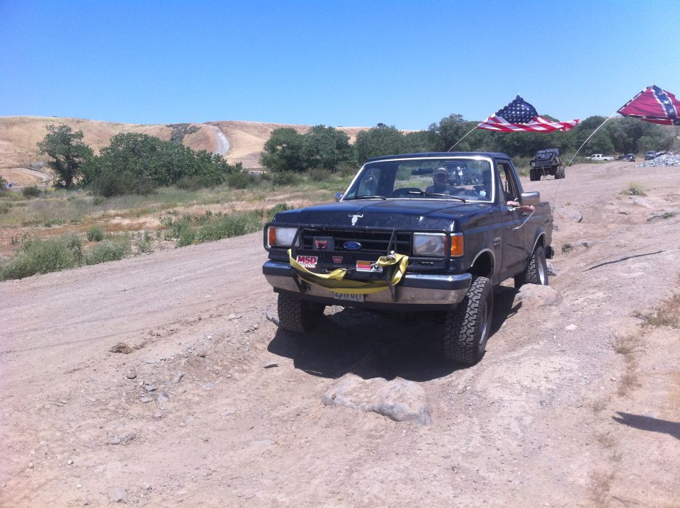 1990 Ford Bronco front view, dark blue, off-roading with flags