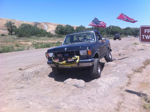 1990 Ford Bronco - Black Ford Bronco navigates a rocky off-road course, flying two flags from its antenna.