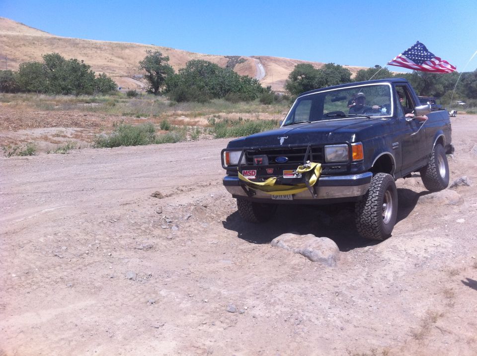 Black Ford Bronco driving over rocks with American flag on back