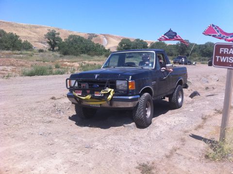 1990 Ford Bronco - 1990 Ford Bronco parked off-road with American and Confederate flags flying.