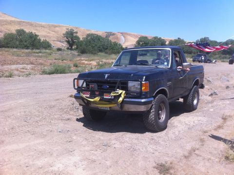 1990 Ford Bronco - A black Ford F-150 pickup truck is seen driving on a dirt road with an American flag attached to its antenna.