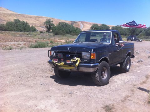 1990 Ford Bronco - A black Ford F-Series truck is parked off-road with an American flag flying in the background.