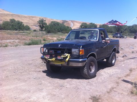 1990 Ford Bronco - This black Ford F-150 pickup truck is equipped with an aftermarket bumper and an American flag.