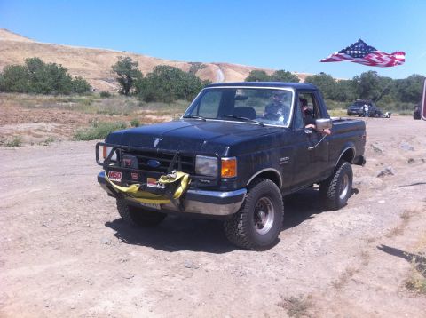 1990 Ford Bronco - A 1990 Ford Bronco is shown off-road with an American flag kite in the sky.