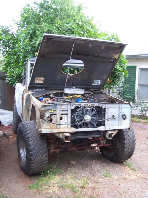 1973 Ford Bronco - The front of a classic Ford Bronco is shown with its hood raised, revealing the engine compartment and cooling fan.