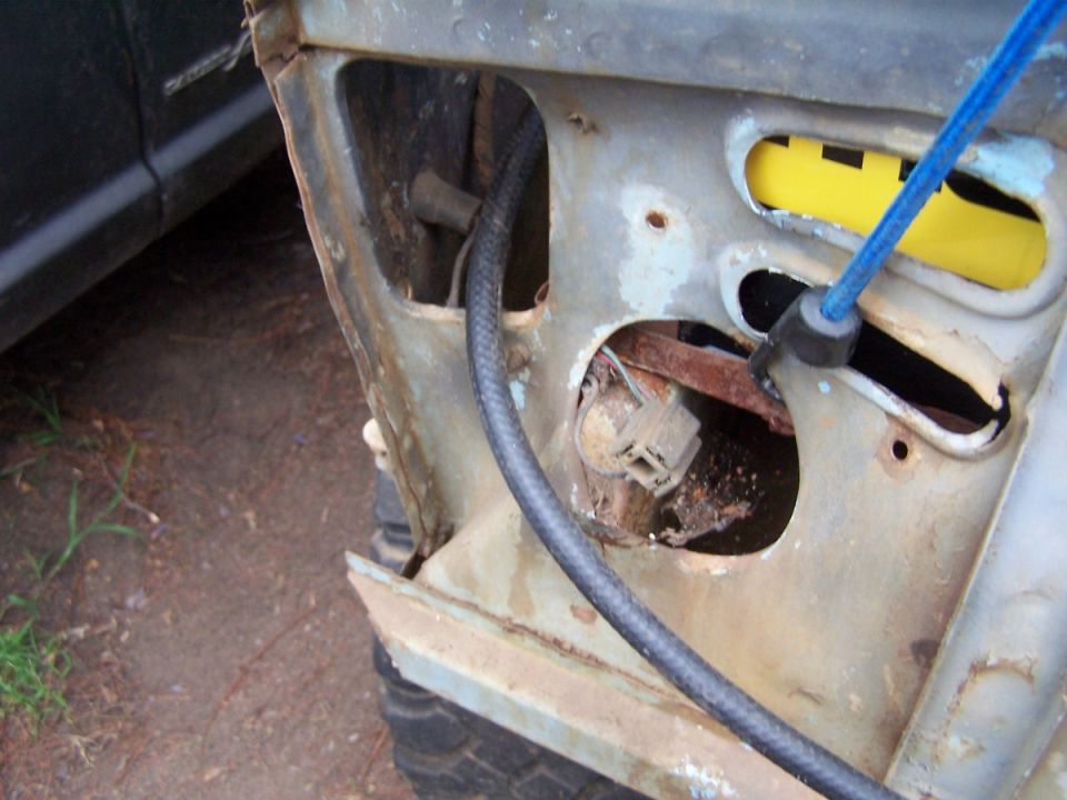 Close-up of rusted vehicle panel with exposed wiring and a blue cable