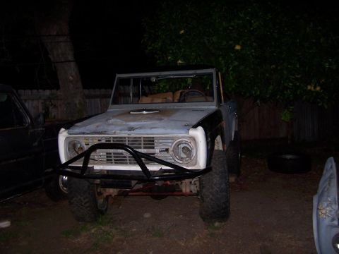 1973 Ford Bronco - A gray Ford Bronco sits in a yard at night, showing its front end with a custom bumper.