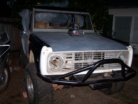 1973 Ford Bronco - A 1973 Ford Bronco is parked outside with a primer gray hood and a black bumper. The headlights are missing.