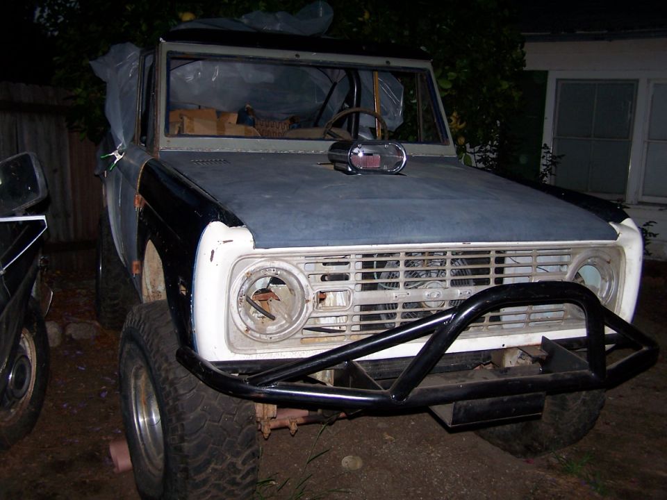 1973 Ford Bronco front view, primer gray hood, black bumper, missing headlights