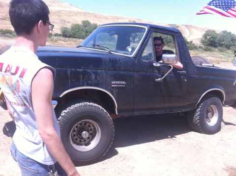 1990 Ford Bronco - A black 1990 Ford Bronco is seen from the front-three-quarter angle with two people present.