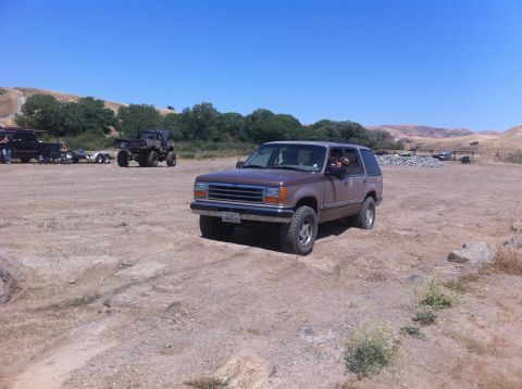 1990 Ford Bronco - Brown Ford Explorer parked in a dirt lot with other vehicles visible in the distance.