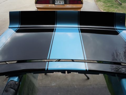 1972 Chevrolet Camaro - A car hood with racing stripes is shown, with the rear of another car visible in the background.