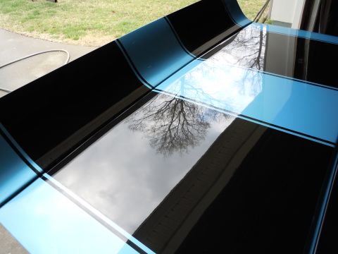 1972 Chevrolet Camaro - A car hood with blue and black racing stripes is shown, reflecting a tree and sky.