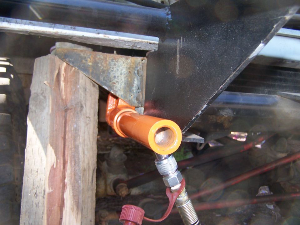 Close-up of a hydraulic line connected to a metal bracket on a vehicle frame, supported by a wooden block