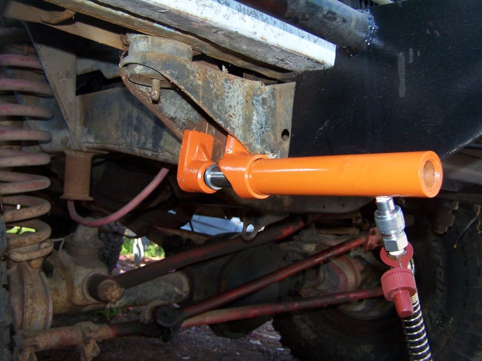 Close-up of an orange suspension component attached to a vehicle's frame, with suspension springs and steering linkage visible