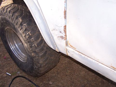 1973 Ford Bronco - Close-up of a white vehicle's fender and door panel, showing rust and a large tire.
