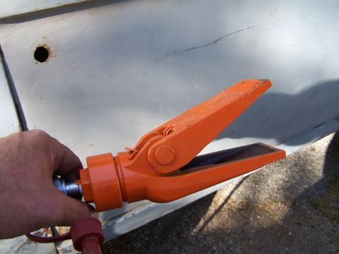 1973 Ford Bronco - A close-up shows an orange hydraulic spreader tool being held by a hand against a weathered gray surface.