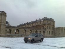 1991 Ford LTD Crown Victoria - A silver Jeep Grand Cherokee sits in a snowy courtyard before a grand, historic building under an overcast sky.