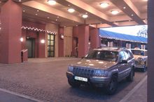 1991 Ford LTD Crown Victoria - A Jeep Grand Cherokee is parked at the entrance of a building, with a taxi visible behind it.